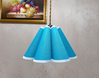 Può includere: Un paralume per lampada in tessuto blu e bianco con un design plissettato. Il paralume è appeso a un cavo.