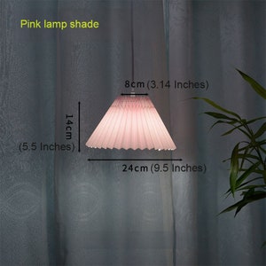 May include: A pink pleated lampshade with a diameter of 9.5 inches and a height of 5.5 inches. The lampshade is hanging from a white cord.
