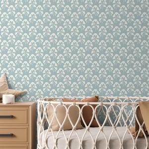 May include: A nursery scene featuring a light blue patterned wallpaper with a repeating white floral design. A wooden dresser with a star-shaped pillow, a stuffed elephant, and a crib with pillows and a blanket are in the foreground.