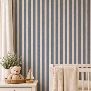 May include: A nursery setting with a white cot and a cream blanket. A white chest of drawers holds a teddy bear in a woven basket and a wooden sailboat. The backdrop is a blue and white striped wallpaper.
