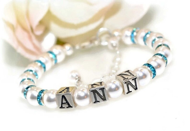 White pearl flower girl bracelet. Each pearl is spaced with silver plated aquamarine crystal rondelles. The name ANN is spelled with sterling silver block letters. Closes with a sterling silver lobster claw clasp with extender chain.