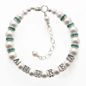 May include: A pearl bracelet with the name "ANDRE" spelled out in silver letter beads. The bracelet features white pearls, interspersed with turquoise-colored rhinestone spacers, and a silver chain clasp.
