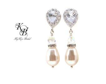 May include: A pair of elegant drop earrings. Each earring features a pear-shaped, clear cubic zirconia stone surrounded by smaller stones. Below the top stone is a crystal bead and a large, cream-colored pearl. The earrings are on a white background.