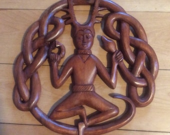 May include: A wooden carving of a Celtic deity with antlers and a snake, surrounded by a knotwork design.