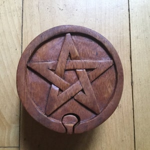 May include: A wooden box with a carved pentagram design. The box is round and has a hinged lid.