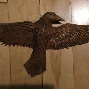 May include: A wooden carving of a brown bird with its wings spread out. The bird is in flight and has a detailed carving of its feathers.