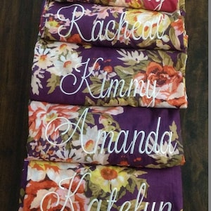 May include: Five purple robes with floral patterns and white embroidered names: Becky, Rachel, Kimmy, Amanda, and Katelyn.