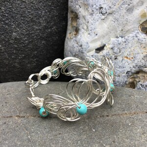 May include: Silver wire bracelet with turquoise beads. The bracelet is made of a series of interconnected loops and is decorated with turquoise beads.