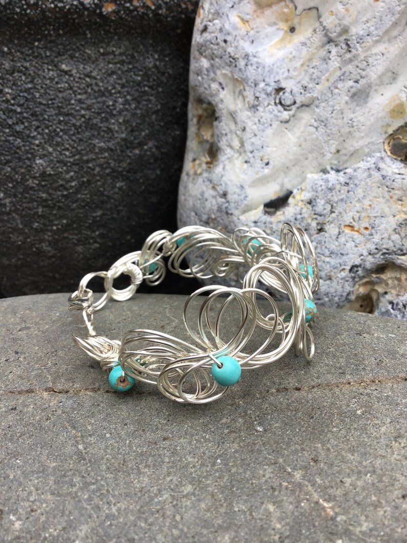 May include: Silver wire bracelet with turquoise beads. The bracelet is made of a series of interconnected loops and is decorated with turquoise beads.