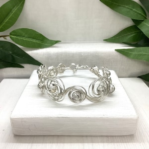 May include: Silver wire bracelet with small silver beads. The bracelet is made of wire that is twisted into a spiral pattern. The beads are evenly spaced along the bracelet.