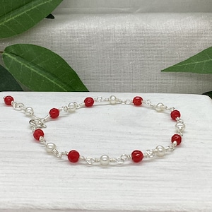 May include: A delicate bracelet with alternating red and white beads. The bracelet is made with silver wire and features a clasp closure.