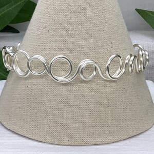 May include: Silver wire choker necklace with a wavy, looped design.