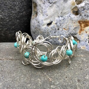 May include: A silver wire bracelet with turquoise beads. The bracelet is made of many small, intertwined loops of wire.