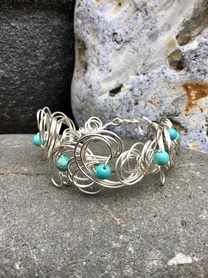May include: A silver wire bracelet with turquoise beads. The bracelet is made of many small, intertwined loops of wire.