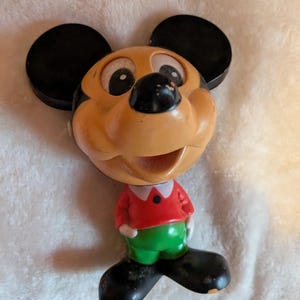 May include: Vintage Mickey Mouse bobblehead figurine. The figure features a tan face with black ears, a black nose, and a red shirt with green pants. The bobblehead is a classic Disney collectible.
