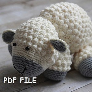 May include: A crocheted white and gray sheep plush toy with black eyes. The sheep has a textured, bumpy surface. The toy is lying on a light wood surface.  PDF FILE.