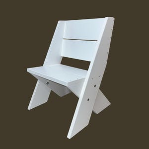 May include: White wooden chair with a simple design. The chair has a straight back with a horizontal slat and a slightly angled seat. The legs are angled and cross in the middle.