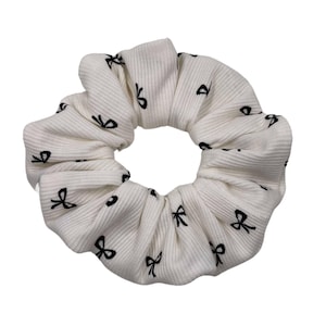 Puede incluir: Scrunchie blanco con un patrón de lazo negro.
