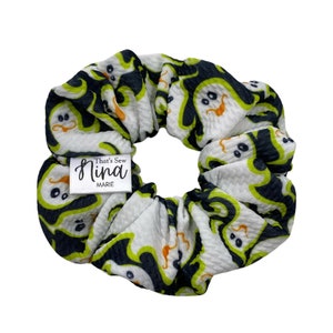 Op de afbeelding: Een witte scrunchie met een zwart en groen spookpatroon. De scrunchie heeft een klein label met de tekst "That's Sew Nina Marie".