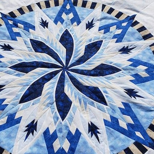 May include: A blue and white quilt with a geometric starburst pattern. The quilt is made of various shades of blue and white fabric, and the starburst pattern is created by piecing together different shapes of fabric.