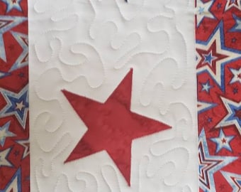 May include: A white fabric panel with a quilted design of swirling lines. Three stars are appliqued on the panel, one red and two blue with white stars. The stars are arranged vertically down the center of the panel.