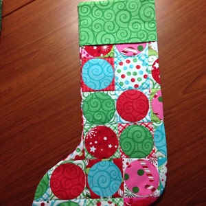 May include: A red, green, blue, and white Christmas stocking with a patchwork design of circles and swirls.