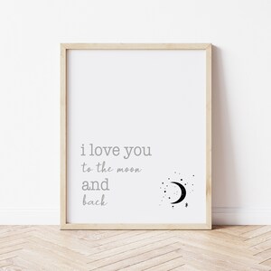 Op de afbeelding: Een ingelijste print met de tekst "i love you to the moon and back" in grijze letters. Een zwarte halve maan en sterrenafbeelding staat rechts van de tekst. De lijst is van licht hout en de achtergrond is wit.