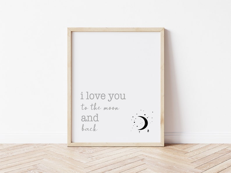 Op de afbeelding: Een ingelijste print met de tekst "i love you to the moon and back" in grijze letters. Een zwarte halve maan en sterrenafbeelding staat rechts van de tekst. De lijst is van licht hout en de achtergrond is wit.