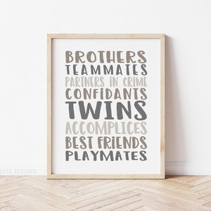 May include: A framed print with the words "Brothers, Teammates, Partners in Crime, Confidants, Twins, Accomplices, Best Friends, Playmates" in a gray and brown color scheme. The text is arranged in a vertical column with the word "Twins" in a larger font size.