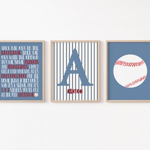 Może przedstawiać: Trzy wydruki w stylu baseballowym do pokoju dziecięcego lub pokoju niemowlęcia. Pierwszy wydruk zawiera tekst piosenki "Take Me Out to the Ballgame". Drugi wydruk przedstawia niebieską literę "A" na biało-niebieskim paskowanym tle z napisem "Ashton" poniżej. Trzeci wydruk przedstawia białą piłkę baseballową z czerwonymi szwami na niebieskim tle.