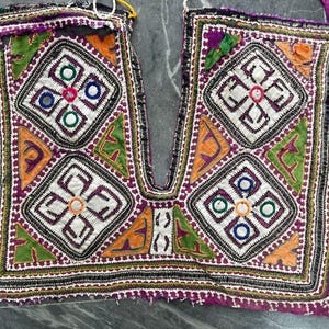 May include: A textile panel featuring intricate embroidery in purple, green, orange, and white. The design includes four diamond-shaped motifs with circular mirror accents, geometric patterns, and decorative borders with multi-colored fabric patches.