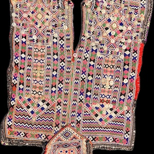 Könnte beinhalten: Aufwendig besticktes Textil mit geometrischen Mustern in Pink, Blau, Grün und Weiß. Kleine, runde Verzierungen akzentuieren das Design. Es hat eine zentrale Öffnung und ein kleineres, angebrachtes Stück.