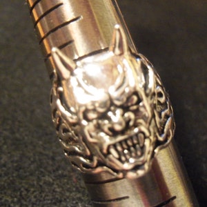 May include: A silver ring with a detailed design of a demon's face with horns and fangs.