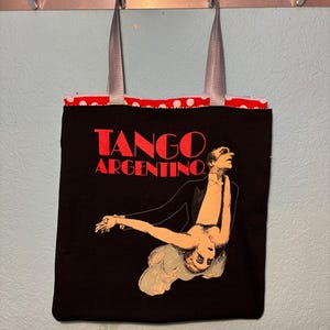 May include: Black tote bag with the words "TANGO ARGENTINO" in red. The bag features an illustration of a dancing couple. The bag has gray straps and a red and white polka dot lining.