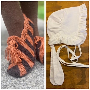 May include: A pair of handmade, striped crochet slippers in brown and orange, with a tassel detail. Next to it is a white bonnet with ruffled edges and long ties, likely for a baby or child. The items are displayed on a wooden surface.