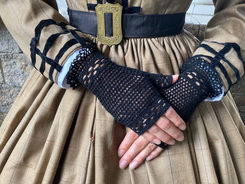 Puede incluir: Guantes sin dedos de crochet negro con un delicado dise&ntilde;o calado. Los guantes se usan sobre un pu&ntilde;o blanco y se combinan con un vestido a cuadros marr&oacute;n. Los guantes son un accesorio elegante.