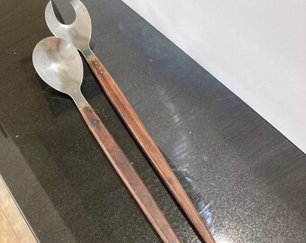 May include: A set of two wooden handled salad servers with stainless steel heads. The server on the left is a spoon and the server on the right is a fork.