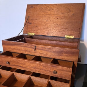 May include: A wooden box with three drawers. The top drawer is open and has a chain attached to the lid. The box has a keyhole and brass hinges. The drawers have brass knobs.