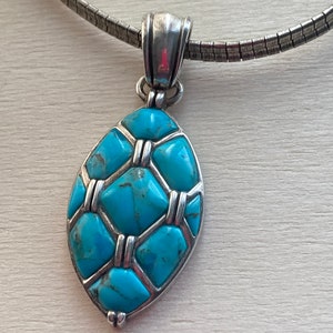 May include: A silver chain necklace with a turquoise pendant. The pendant is oval shaped and features a geometric design with turquoise stones set in silver.