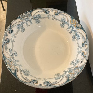 May include: A large white ceramic bowl with a blue and gold floral design. The bowl has a wide rim and a deep well.