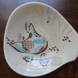 May include: A white ceramic serving dish with a brown and blue bird design. The bird has a brown body with blue wings and a blue tail. The dish has a brown speckled glaze and a brown rim.