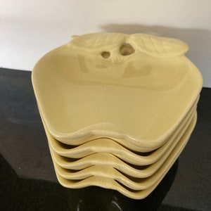 May include: Set of four yellow ceramic apple-shaped serving dishes. The dishes have a raised rim and a leaf design on the top.