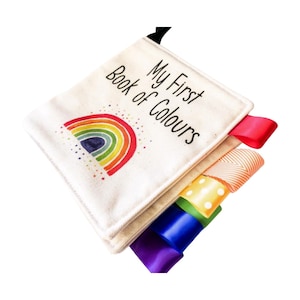 May include: A soft, fabric book for babies and toddlers with the title "My First Book of Colours". The book features a rainbow with stars and has colorful ribbons attached to the pages.