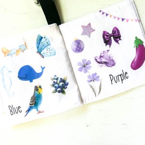 May include: A baby book with colorful illustrations and the words "Blue" and "Purple". The book features a blue whale, a butterfly, a plane, a seahorse, blueberries, a star, a bow, a flower, and an eggplant.