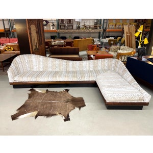 May include: A white and gray patterned sectional sofa with a wooden frame and a brown animal skin rug in front of it.