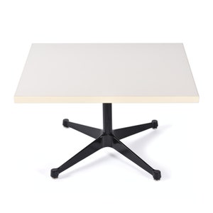 May include: A white square table with a black star-shaped base. The table top has a light beige edge.