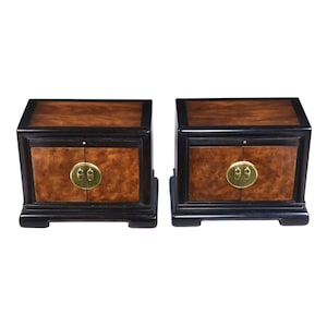 May include: Two matching wooden cabinets with a black frame and a burl wood front. Each cabinet has a brass handle and a dark wood top. The cabinets are rectangular and sit on a black base.