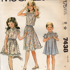 Pode incluir: Padrão de costura McCall's vintage para vestidos de menina. O padrão apresenta ilustrações de três estilos diferentes de vestidos com estampas florais e de bolinhas. O número do padrão é 7438 e o tamanho da menina é 7.