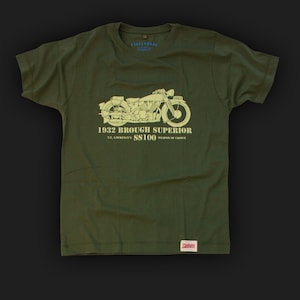 May include: A green t-shirt with a white graphic of a 1932 Brough Superior SS100 motorcycle. The text "T.E. LAWRENCE'S SS100 WEAPON OF CHOICE" is printed below the motorcycle.