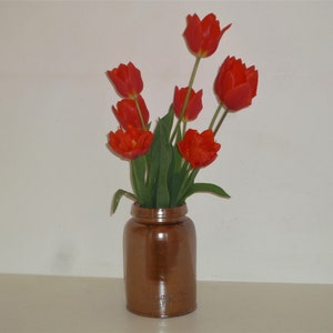 May include: A bouquet of red tulips in a brown ceramic vase.